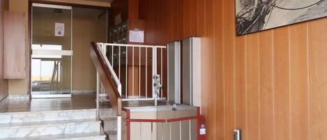 A staircase leading to a landing with a red gate, wooden paneling on the walls, and a painting above the gate.