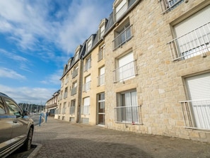 Une rangée de bâtiments en pierre dotés de balcons, une rue pavée et une voiture garée.