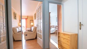 Ein Zimmer mit Holzboden, einem beigefarbenen Sofa, einer Holzkommode und einem Bett mit gestreifter Kopfteil.