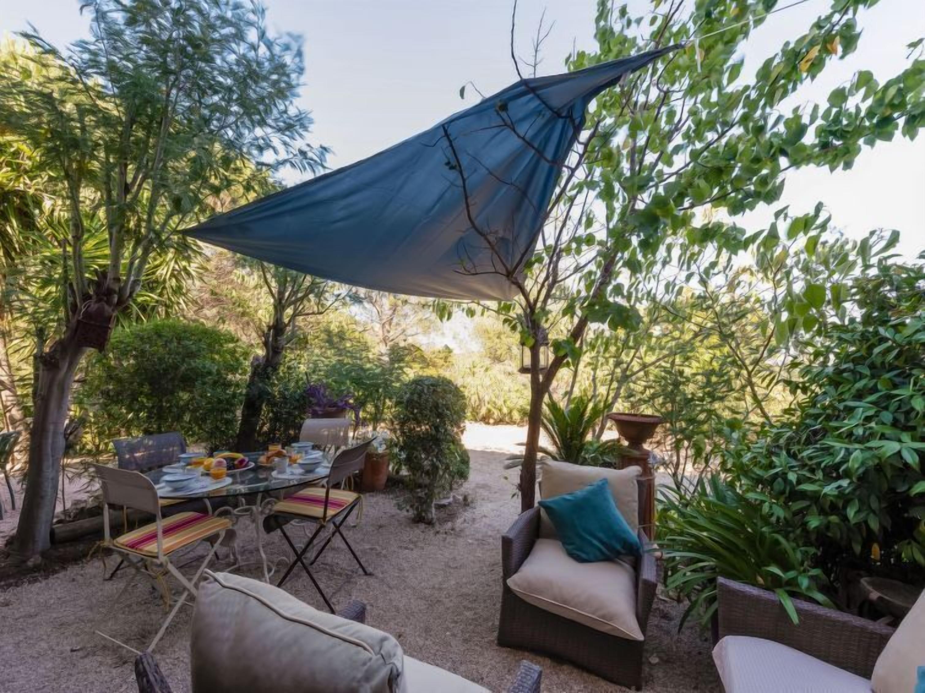 Ein Terrassenbereich im Freien mit Esstisch, umgeben von Korbmöbeln und einem großen Sonnensegel.