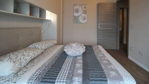 Een slaapkamer met een bed, hoofdeinde, een plank met decoratieve voorwerpen, een schilderij en een deur.