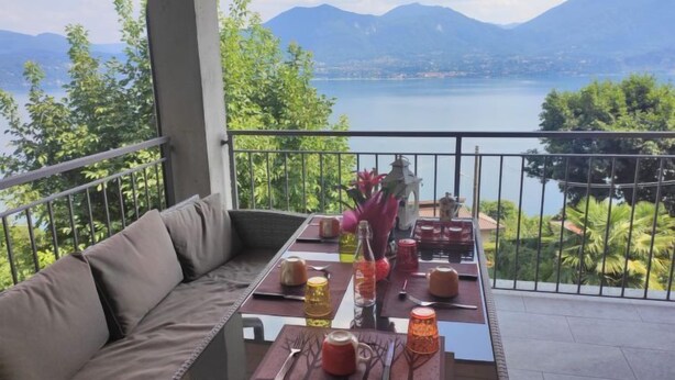 Een balkon met uitzicht op een meer en bergen, ingericht met een bank en een eettafel.