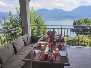 Un balcon avec vue sur un lac et des montagnes, aménagé avec un canapé et une table dressée pour le repas.