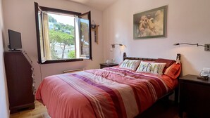 Ein Schlafzimmer mit Bett, Fenster, Gemälde, Lampe und Schreibtisch.