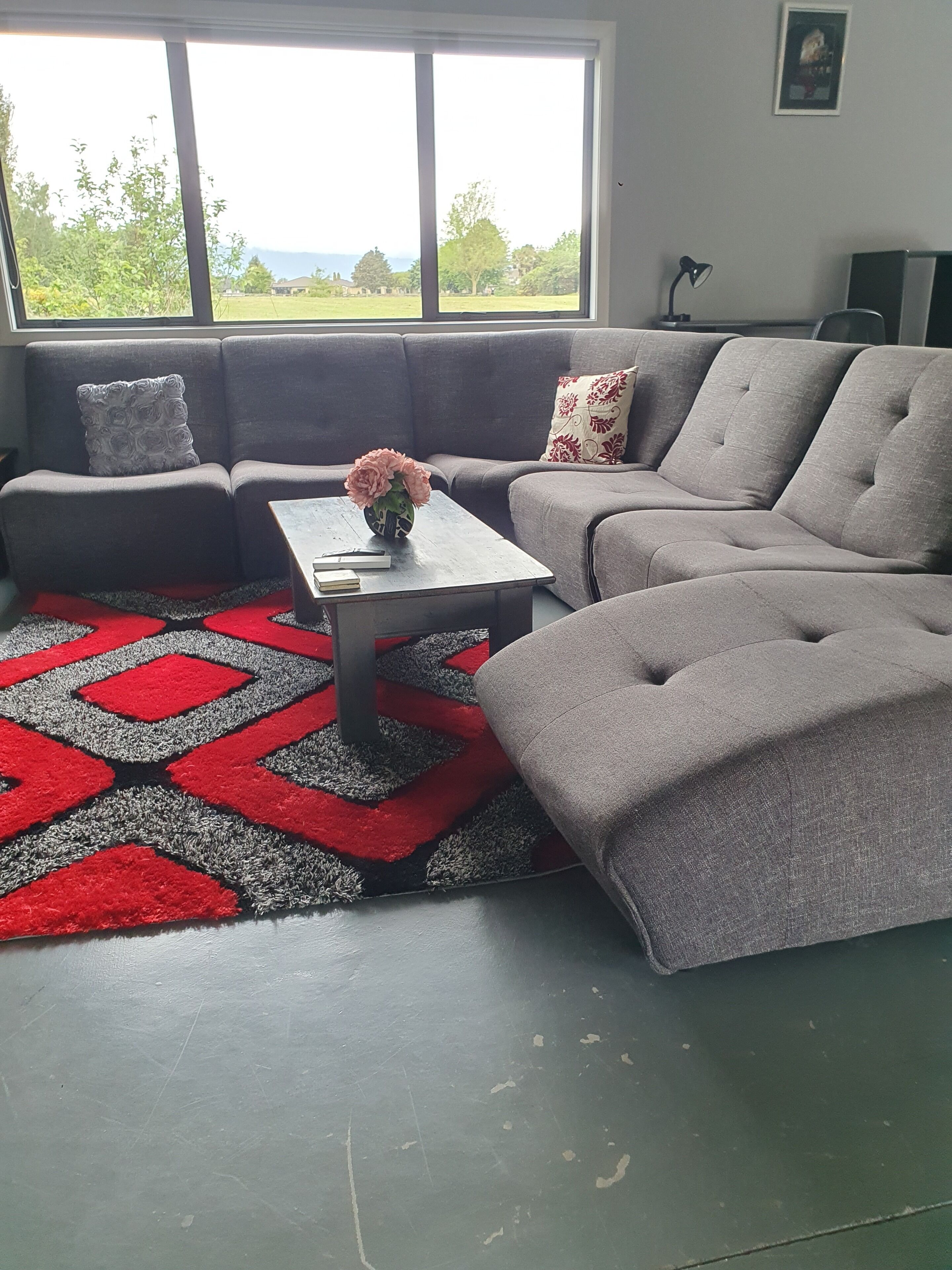 A modern living room with a grey sectional sofa, a coffee table with a vase of flowers, and a red and black patterned rug.