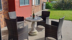 An outdoor patio with wicker chairs and a table, a bottle of champagne, and a large umbrella. - The Red Shed
Large modern studio on two peaceful acres, two minutes from CBD (Matamata)