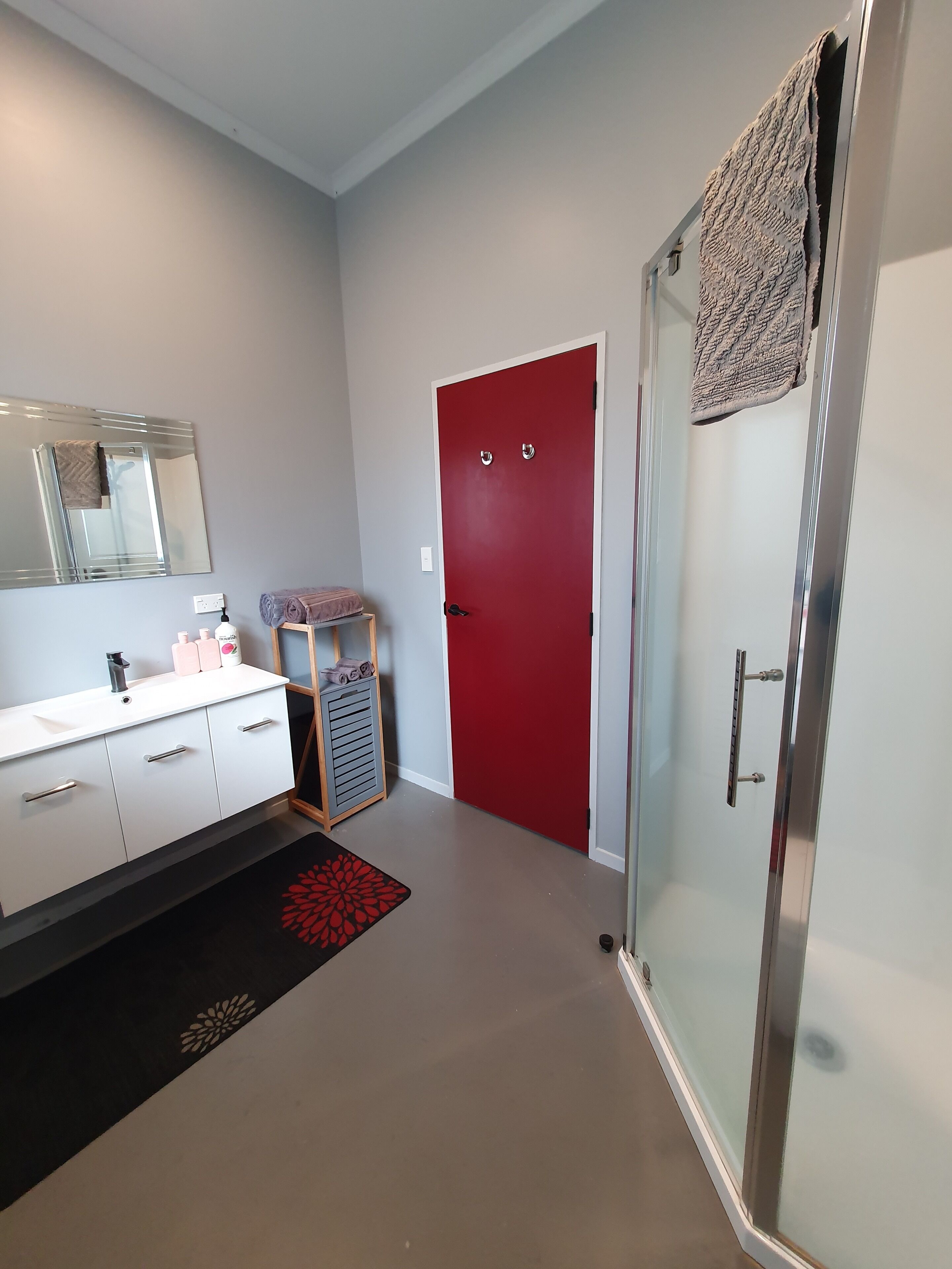 A modern bathroom with a white vanity, a red door, and a glass shower enclosure.