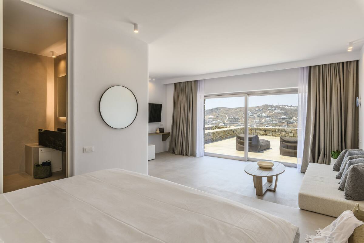 A modern hotel room with a large bed, a seating area with a view, and a balcony with a scenic view.