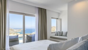 Habitación de hotel con una cama grande, una zona de estar con vistas al mar y un balcón con piscina.