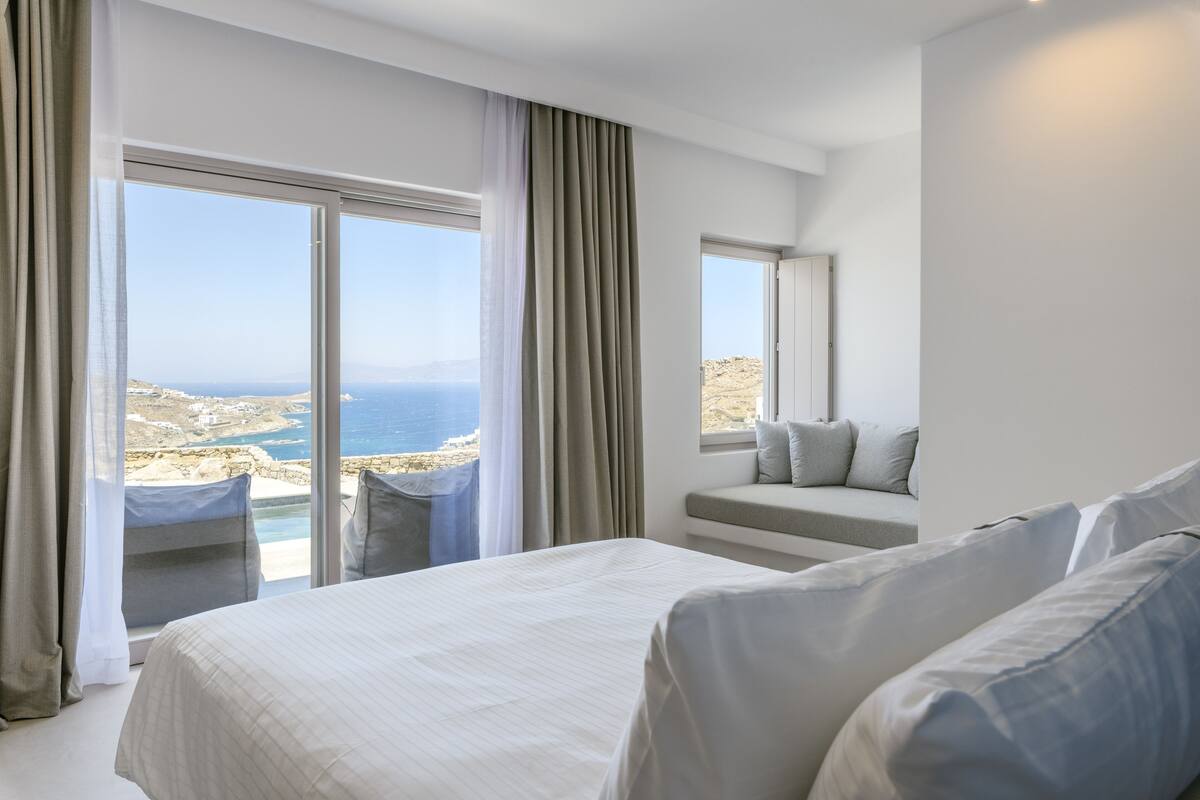 A hotel room with a large bed, a seating area with a view of the sea, and a balcony with a pool.