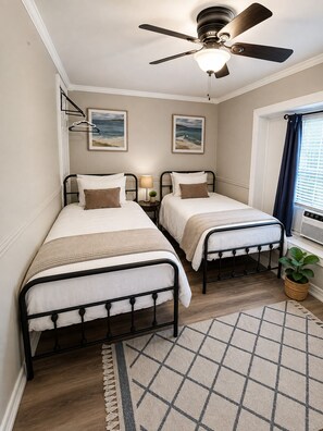 A bedroom with two single beds, a ceiling fan, a window with curtains, and a small plant.