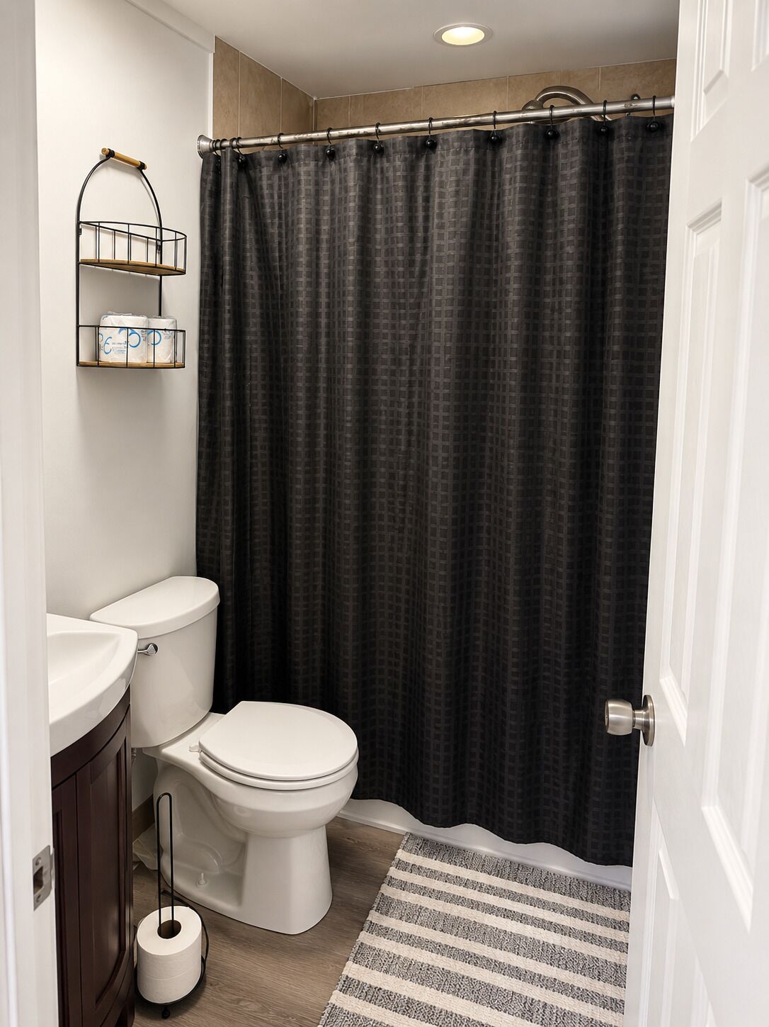 A bathroom with a toilet, a sink, a shower curtain, and a toilet paper holder.
