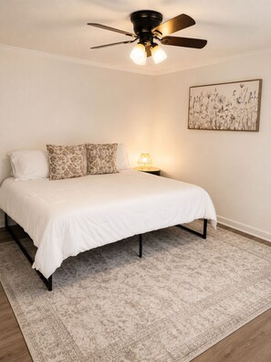 A bedroom with a bed, a nightstand, a lamp, a ceiling fan, and a floral wall art piece.