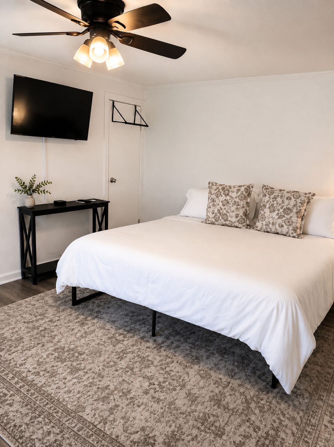 A bedroom with a bed, a desk, a television, and a ceiling fan.