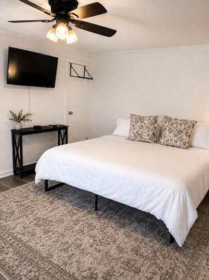 A bedroom with a bed, a desk, a television, and a ceiling fan. - Grandbay Oasis (Grand Bay)