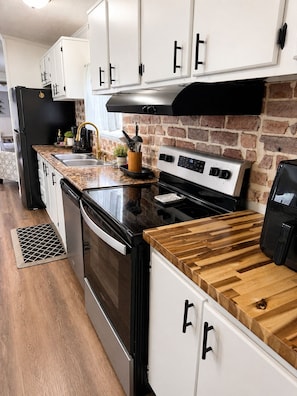 A modern kitchen with white cabinets, a black stove, and a wooden countertop.