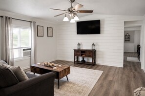 A living room with a ceiling fan, a flat-screen TV, a wooden coffee table, and a sofa. - Grandbay Oasis (Grand Bay)