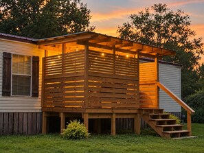 A wooden deck with a staircase leading to a covered area, adjacent to a house with a window and a door.