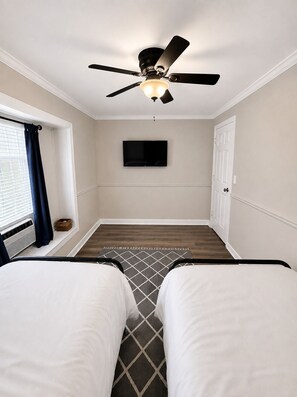 A hotel room with two beds, a ceiling fan, a flat-screen TV, a window with curtains, and a wooden floor. - Grandbay Oasis (Grand Bay)