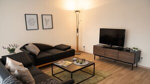 Ein modernes Wohnzimmer mit einer schwarzen Couch, einem Couchtisch, einem Fernseher und einer Stehlampe.