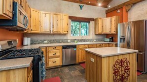 A modern kitchen with wooden cabinets, a central island, stainless steel appliances, and a stone floor.