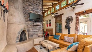 A cozy living room with a stone fireplace, leather sofa, and a flat-screen TV mounted on the wall.