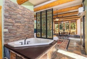 A bathroom with a stone wall, a bathtub, and a view of an outdoor patio with a table and chairs.