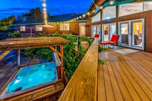 Um deck de madeira com hidromassagem, área de estar externa e uma casa com janelas e portas grandes.
