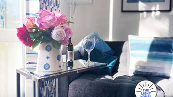A modern living room with a sofa, decorative pillows, a vase with flowers, and a wine bottle on a side table.