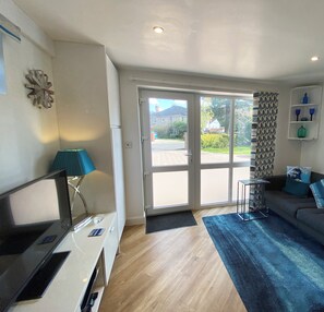 A modern living room with a sofa, a coffee table, and a TV. There is a large window with a view of the outside.