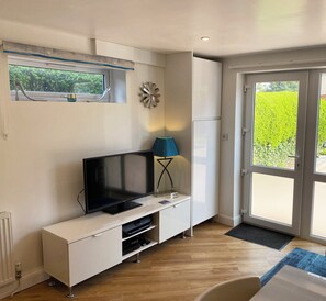 A modern room with a flat-screen TV on a white cabinet, a blue lamp, and a large window with a view of greenery and buildings.