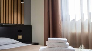 Un lit bien fait, avec une serviette pliée, une tête de lit en bois et une fenêtre avec des rideaux.