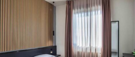 A hotel room with a bed, a desk, a mirror, and a window with curtains.