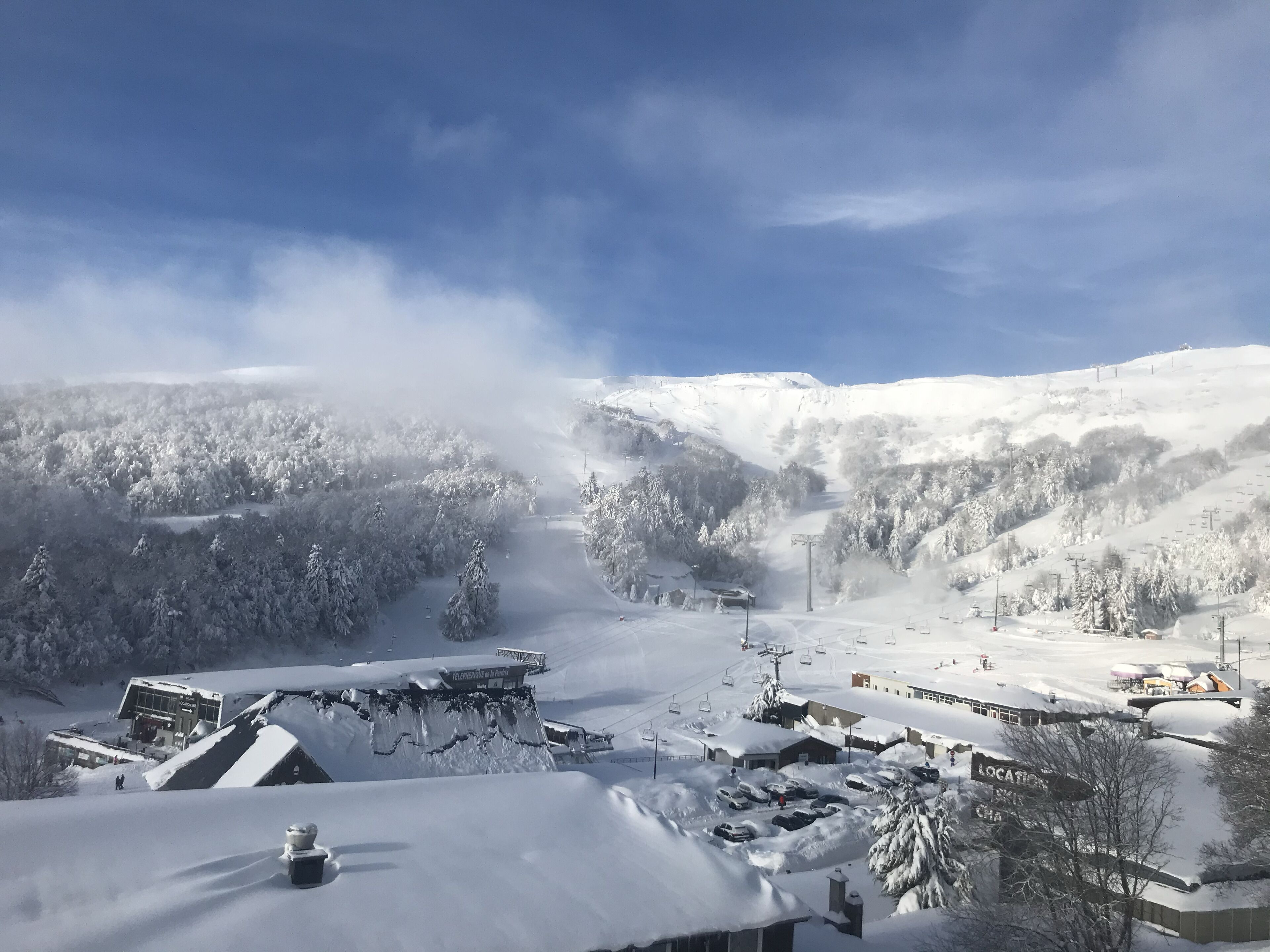 Une station de ski enneigée, avec un télésiège, des bâtiments et un paysage montagneux en arrière-plan.