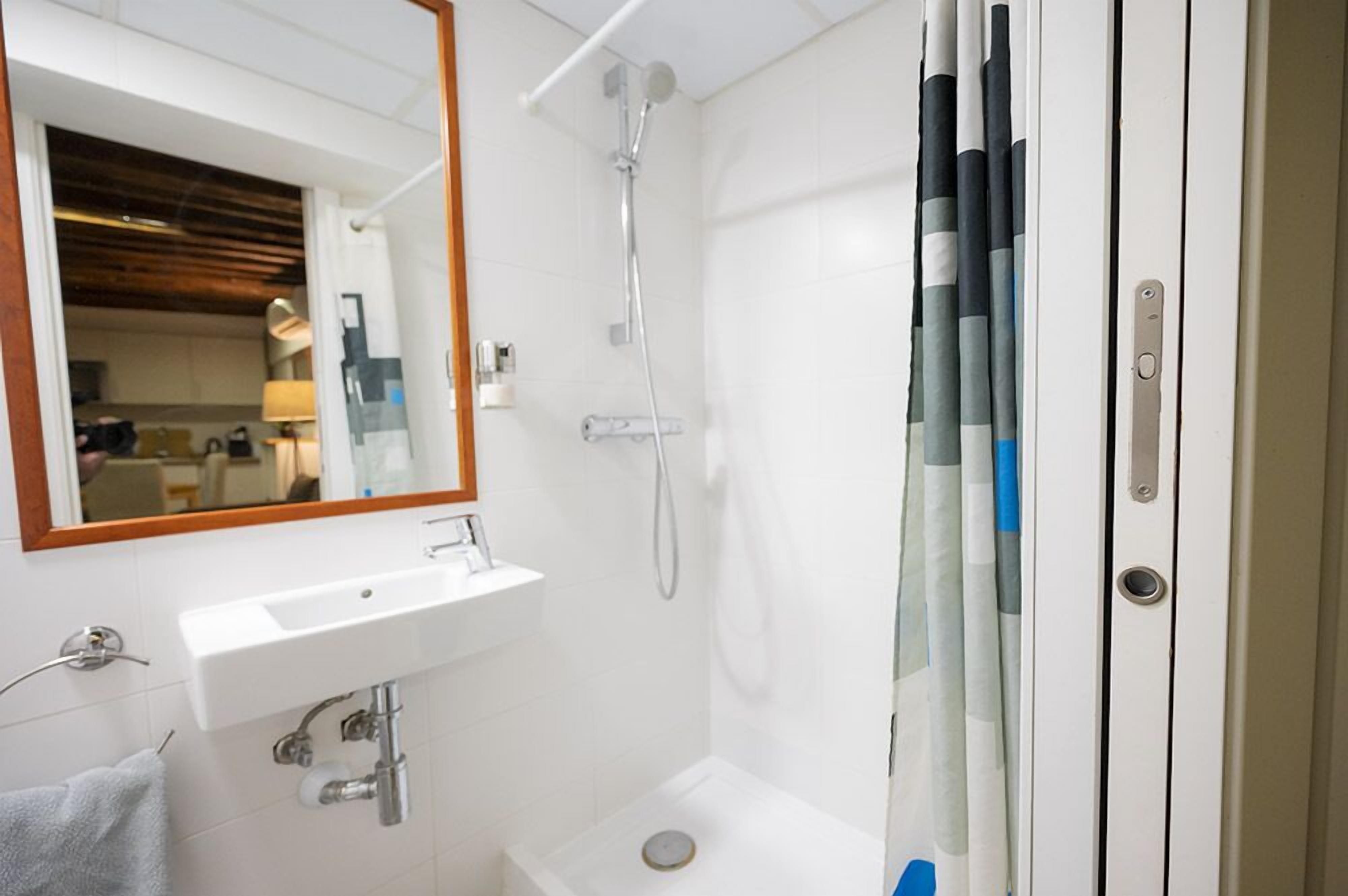 Een moderne badkamer met een wit wastafelmeubel, spiegel en douche.