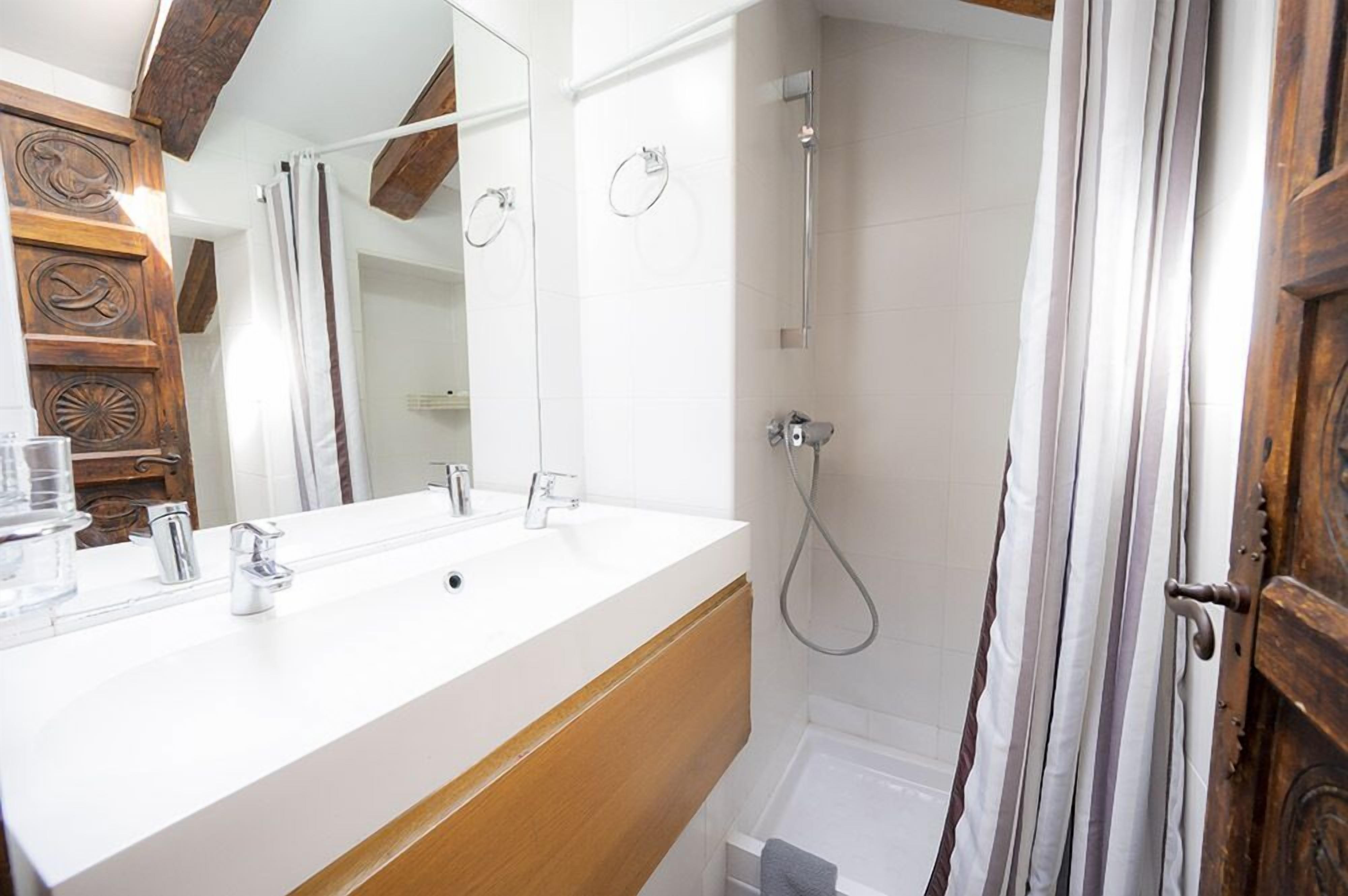 A bathroom with a white sink, wooden vanity, a mirror, a shower, and a wooden door.