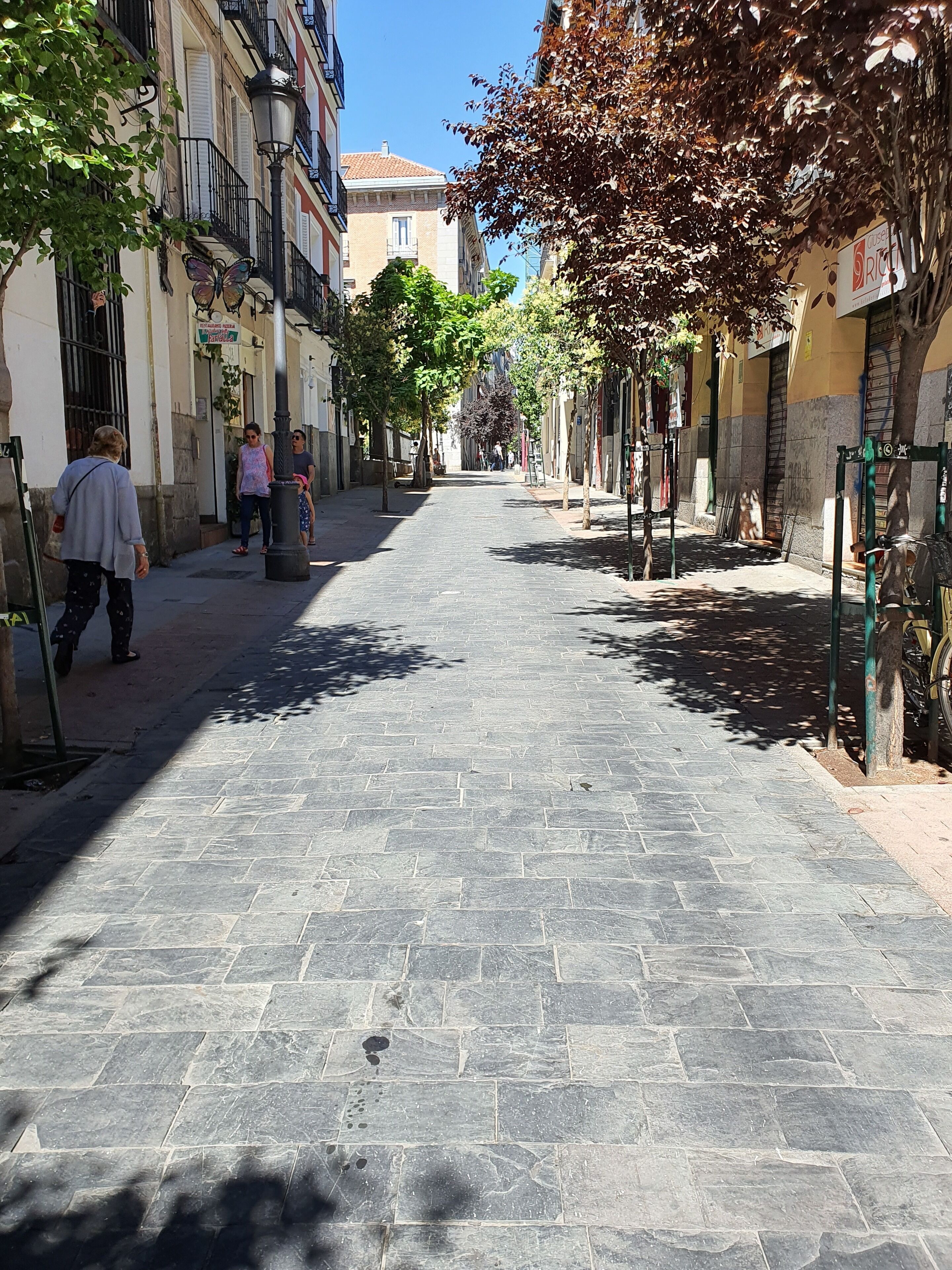 A narrow cobblestone street lined with buildings, some with balconies and signage.