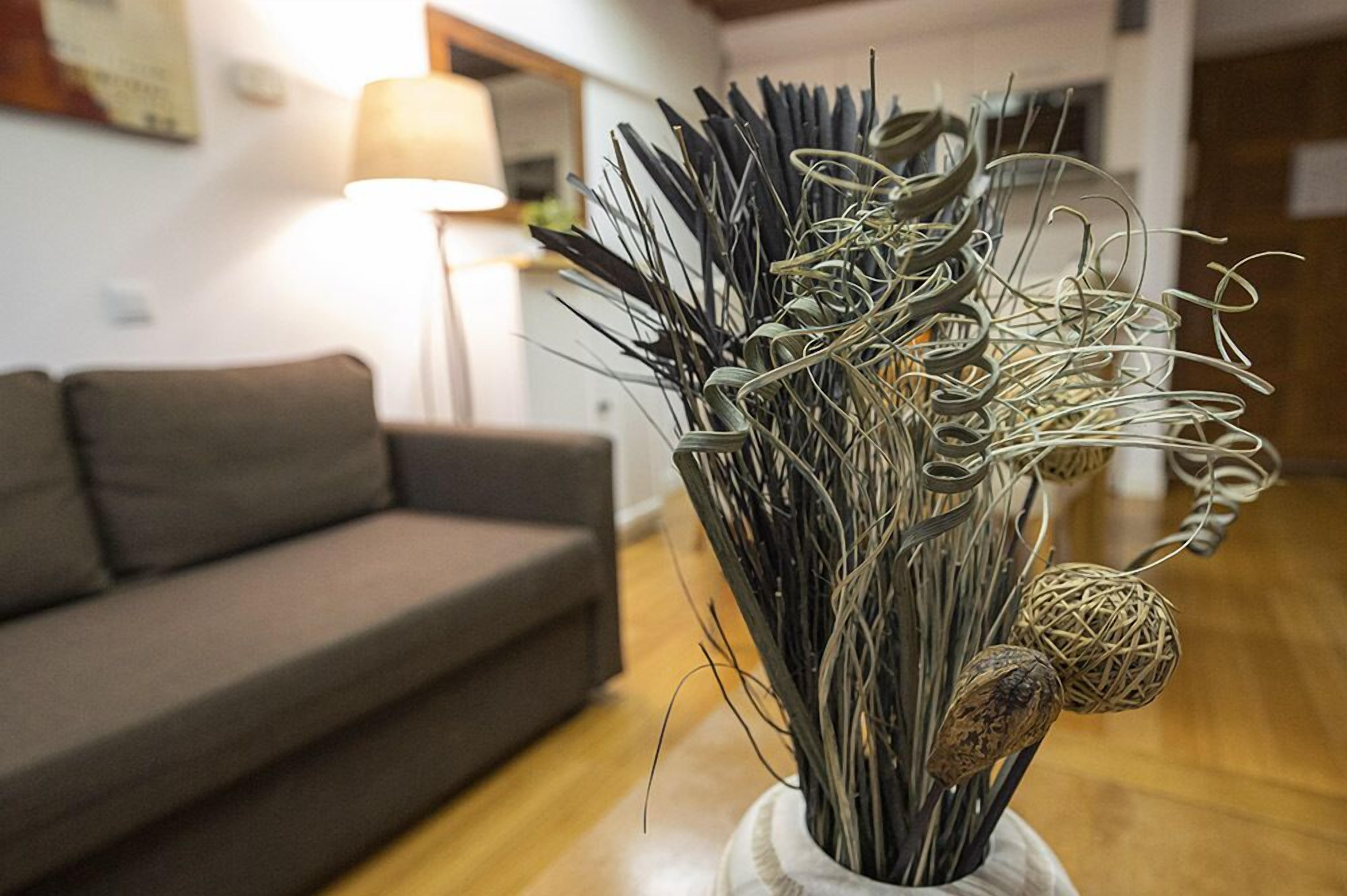 A living room with a grey sofa, a lamp, and a decorative vase with dried plants and wicker balls.