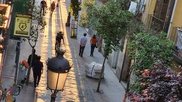 A narrow street lined with trees and buildings, with people walking and a street lamp in the center.