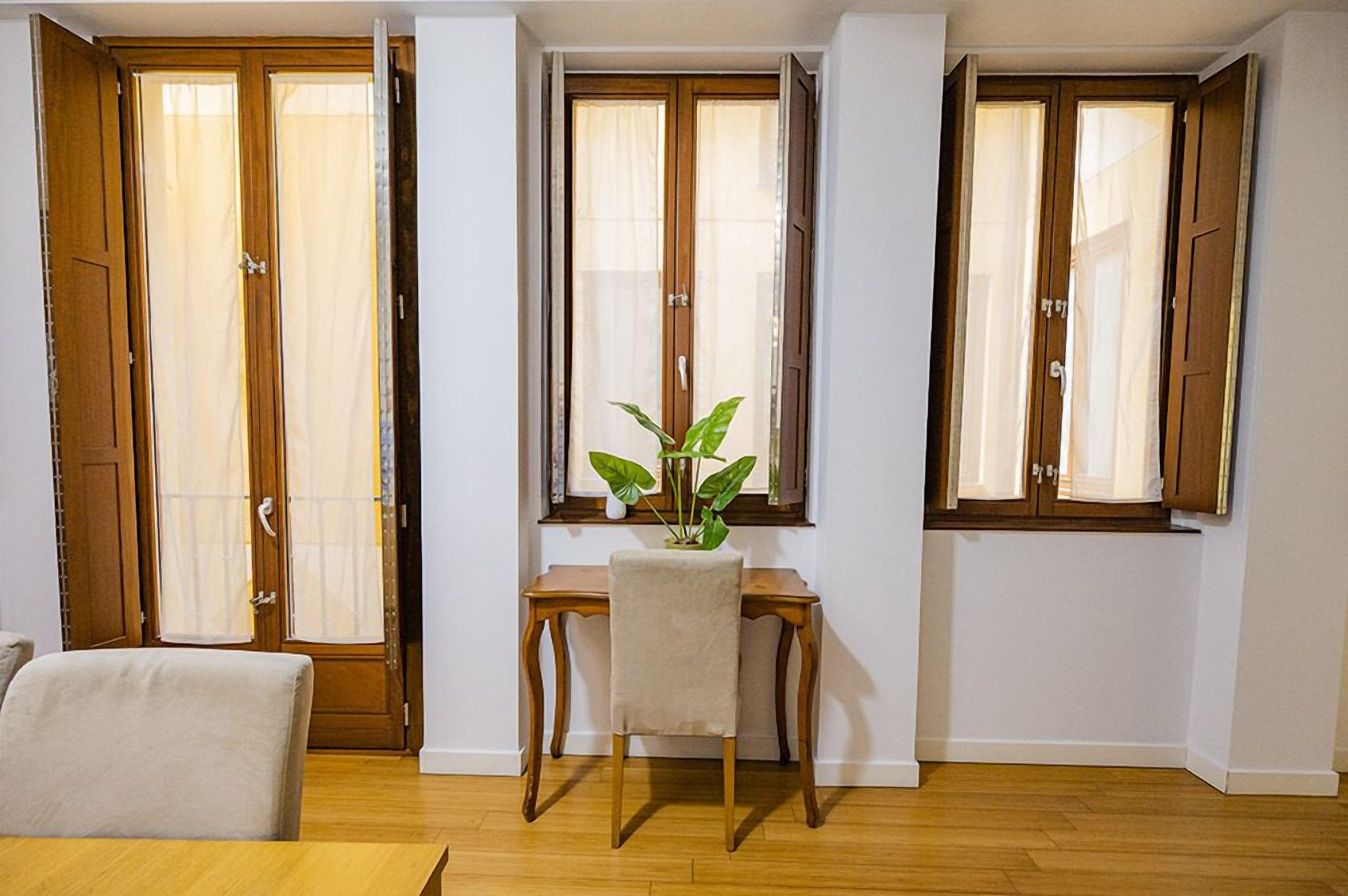 Una habitación con piso de madera, un escritorio con una silla y una planta en maceta.