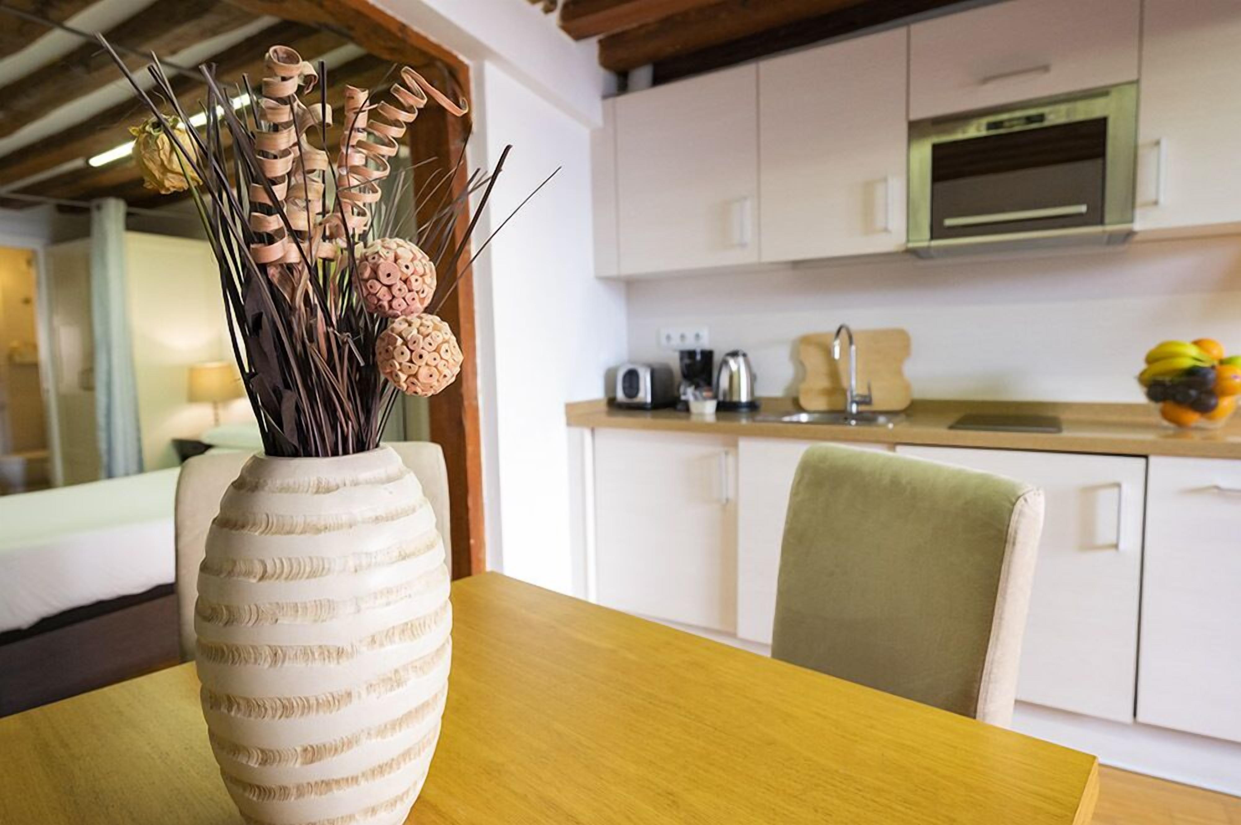 A modern kitchen with white cabinets, a wooden ceiling, and a dining area with a table and a vase of dried plants.