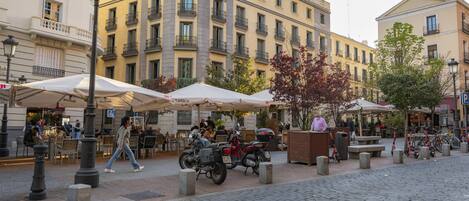 A cobblestone street with outdoor seating, a café, and a building with multiple floors and balconies.