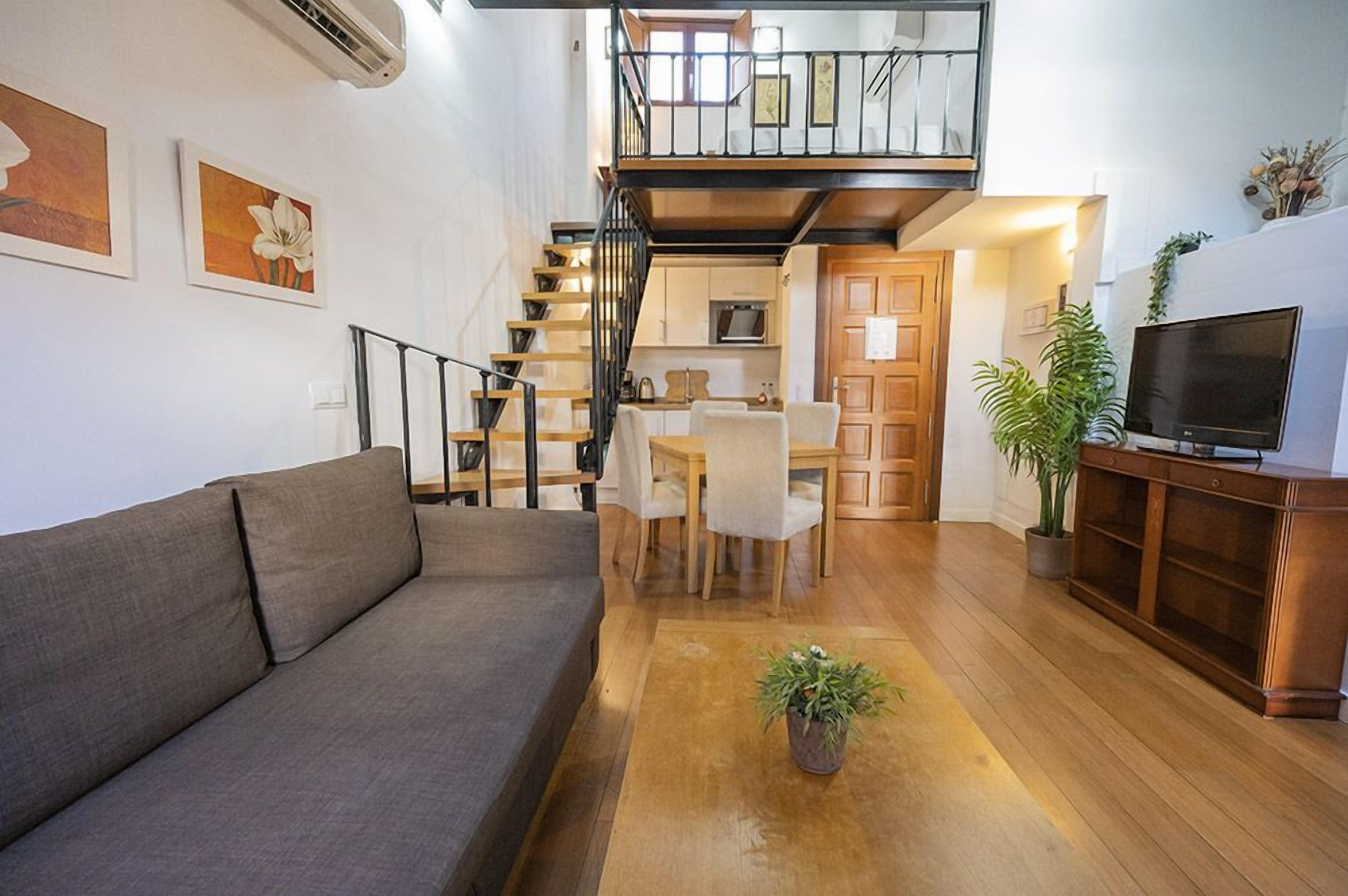 A modern living room with a sofa, a coffee table, a TV, and a staircase leading to an upper level.