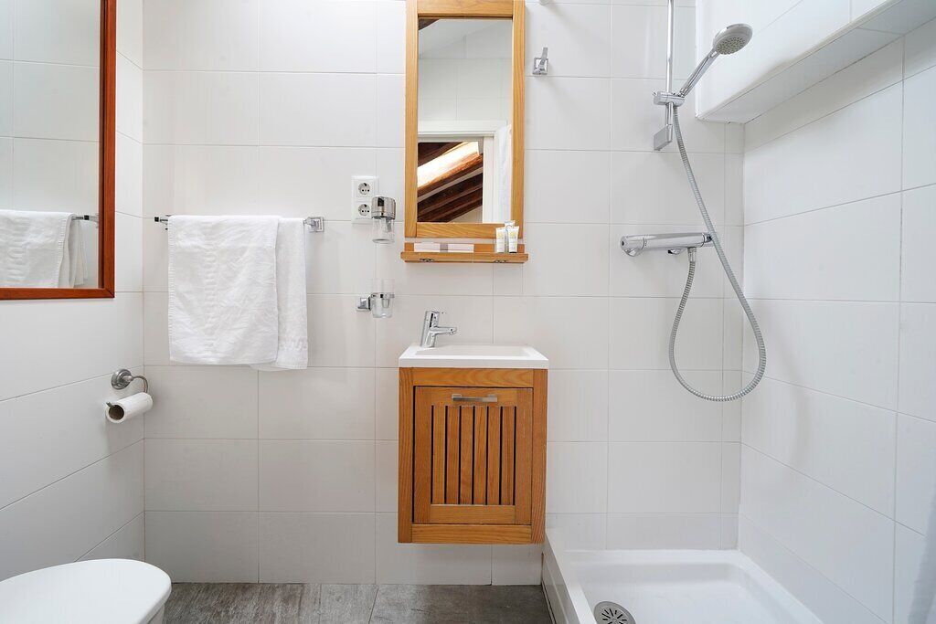 Un baño con inodoro, lavamanos, espejo, toallero, ducha y un armario de madera.