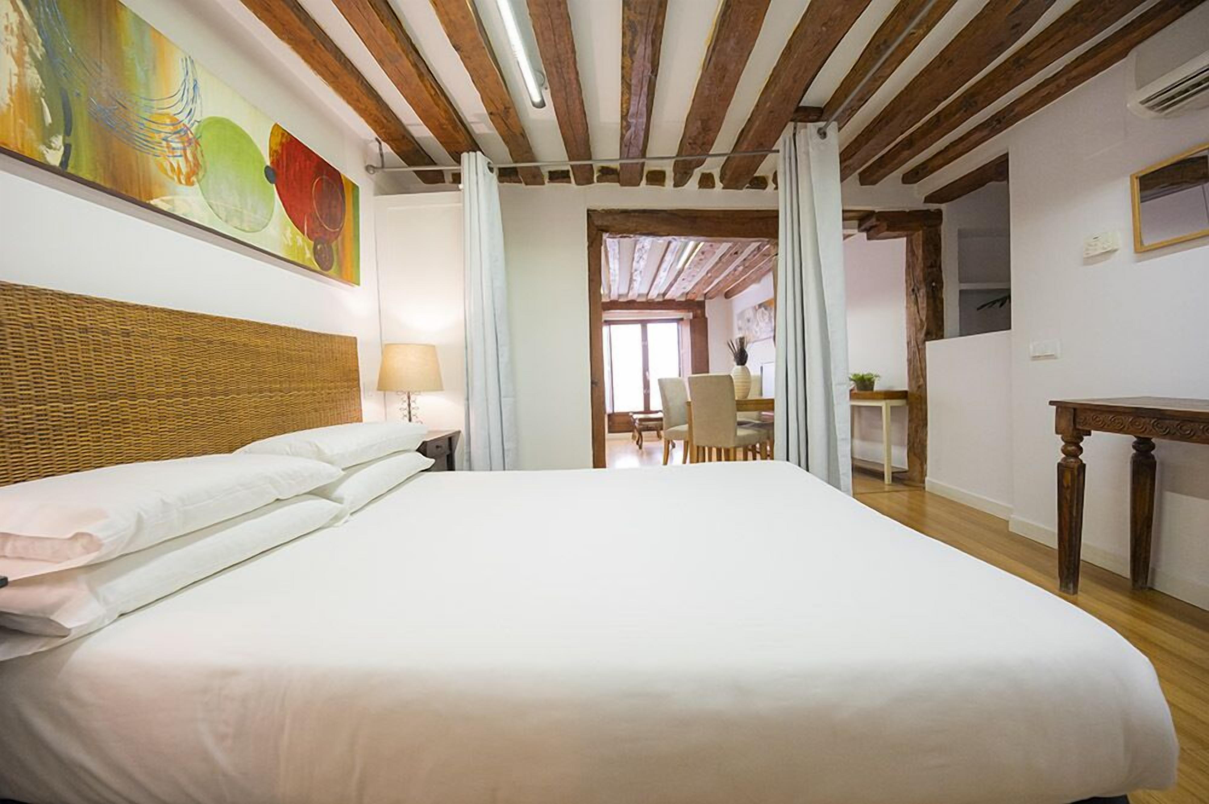 A hotel room with a large bed, wooden ceiling beams, a dining area with chairs, and a table.