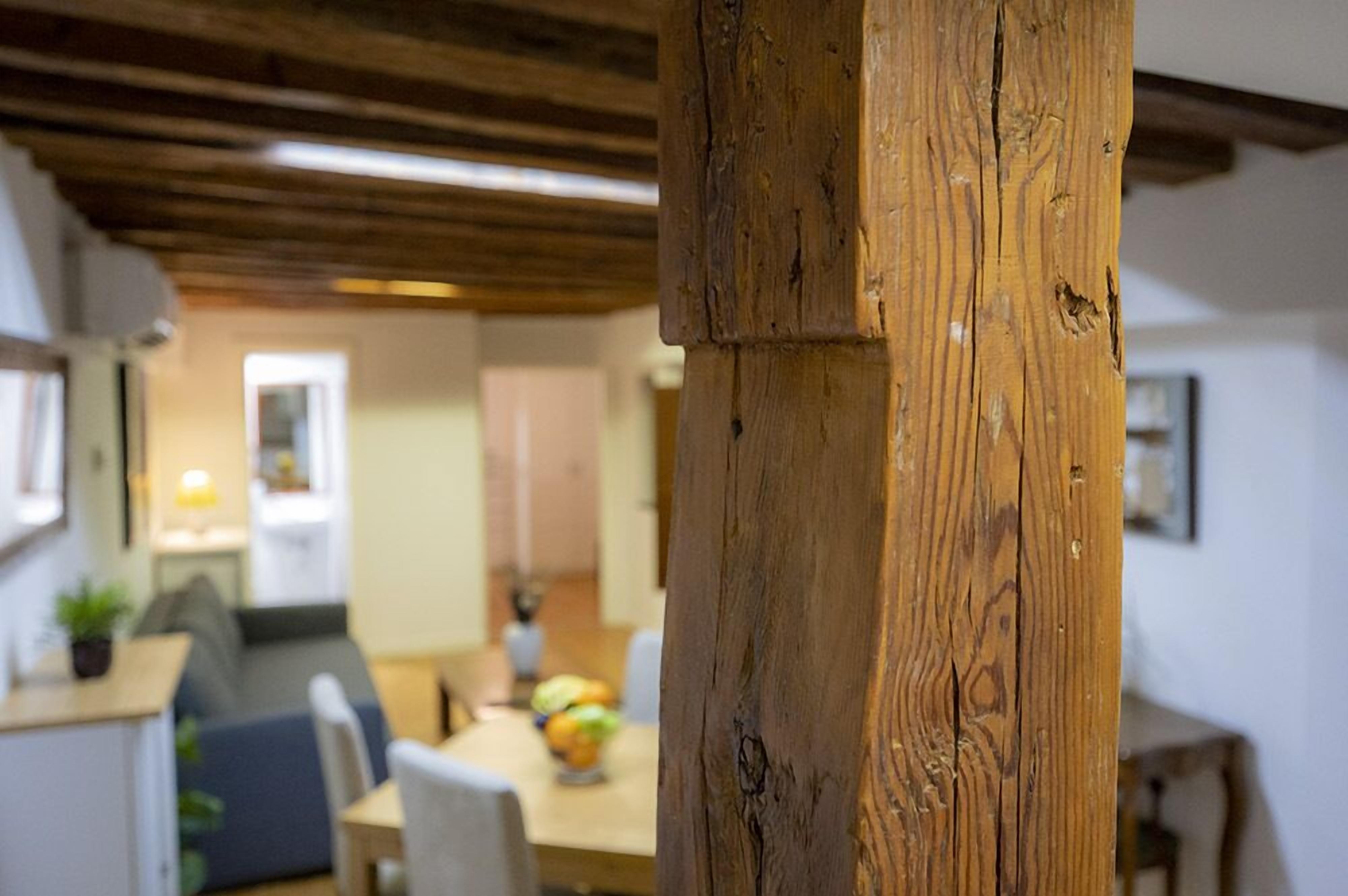 A wooden beam structure in a room with a dining area in the background.