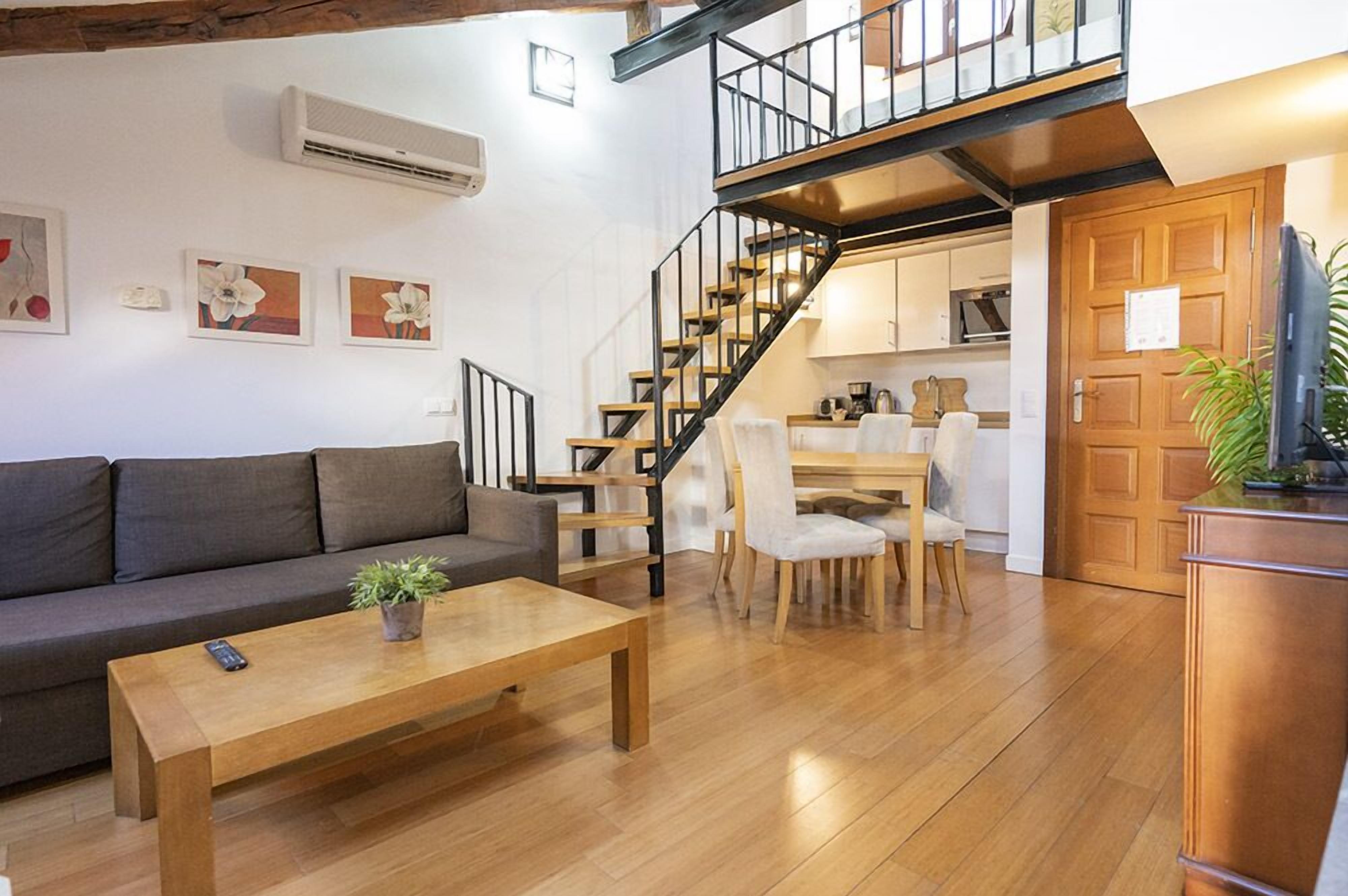 Een moderne woonkamer met een bank, salontafel en een trap naar een keukenhoek.