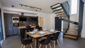 Un espace repas moderne avec une table en bois dressée pour six personnes, des chaises noires et un escalier avec des marches en bois et des rampes en métal.