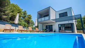Une maison moderne à deux étages dotée d’une piscine, d’un espace salon extérieur et d’un patio couvert.