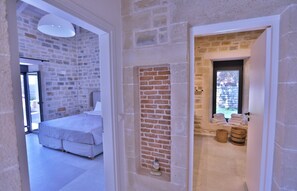 A bedroom with a bed and a large window, a bathroom with a shower and towels, and a stone wall. - new natural stone villa with large pool and great sea views (Prines)